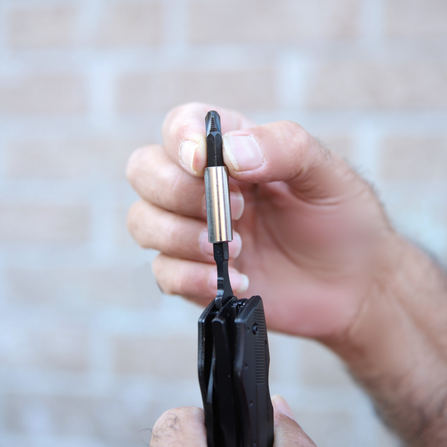 Close-up of hands attaching a magnetic adapter and screwdriver bit to a black Norte heavy-duty multitool, highlighting the 9-piece interchangeable bit set for versatile outdoor tasks.
