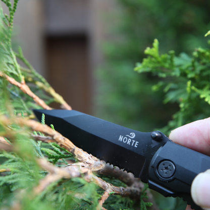 Close-up of a black Norte heavy-duty multitool's partially serrated blade being used in an outdoor setting, highlighting the precision-engineered design and secure locking mechanism.