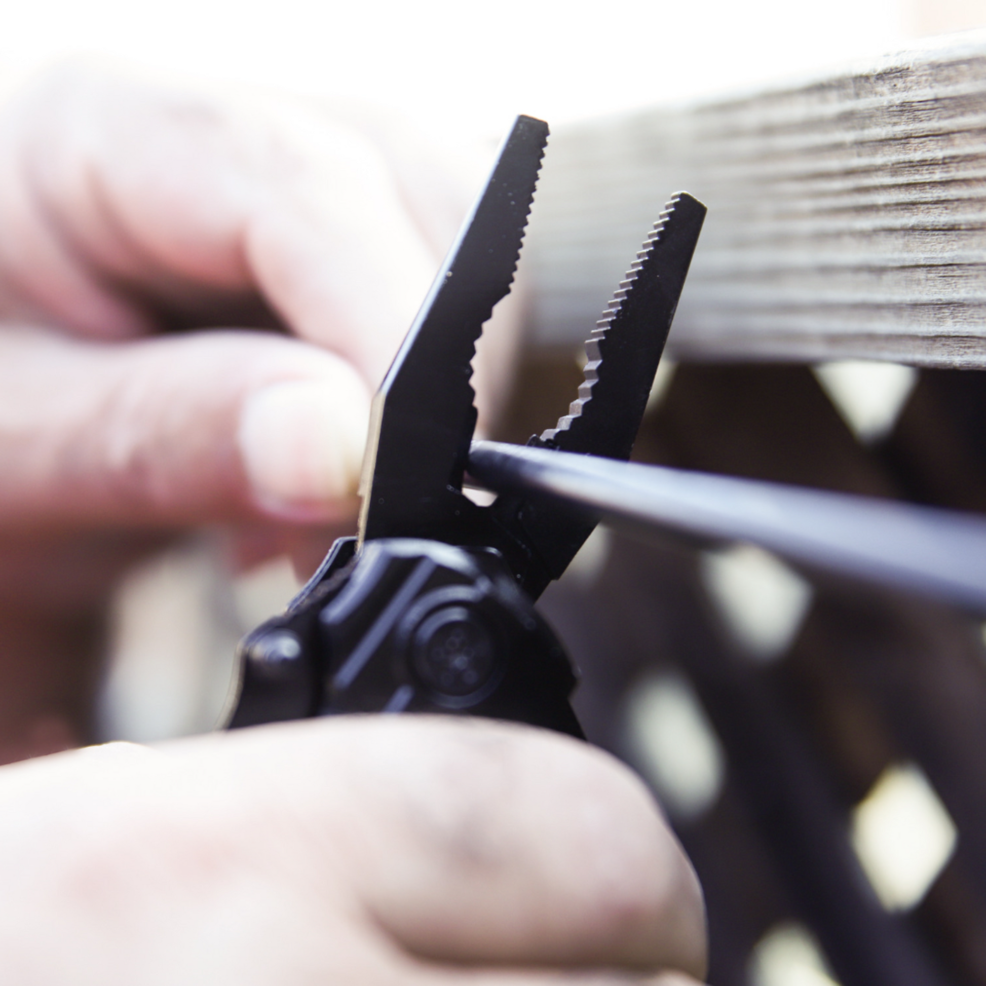 Close-up of a black Norte heavy-duty multitool using needle-nose pliers on a wire, showcasing the ergonomic grip and precision-engineered durability for outdoor tasks.