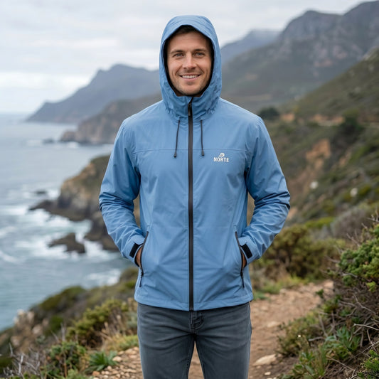 A man wearing a light blue Norte technical hooded jacket with the hood up, standing on a coastal mountain trail.