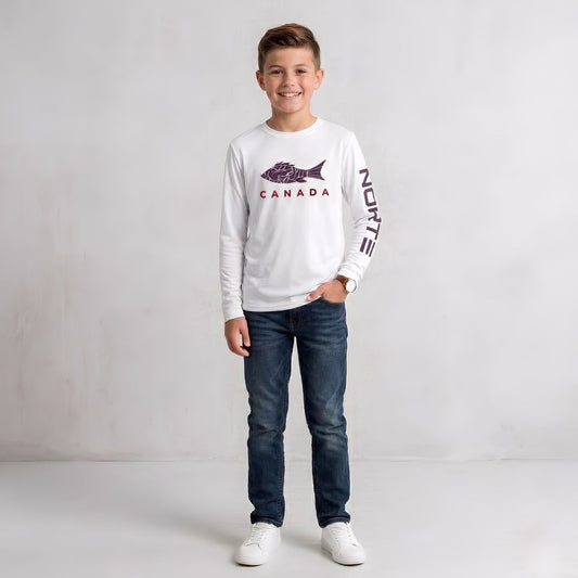 A young boy wearing a white long-sleeve Norte Canada shirt featuring a purple fish graphic on the front, text on the sleeve, dark blue jeans, and white sneakers against a gray studio background.