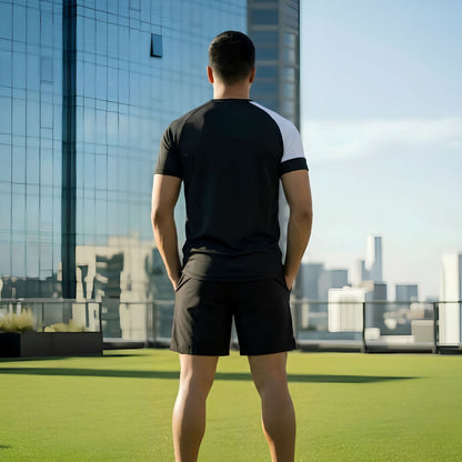 Rear view of a model wearing a Norte branded black short-sleeve athletic t-shirt with a white sleeve and black shorts on a rooftop terrace.