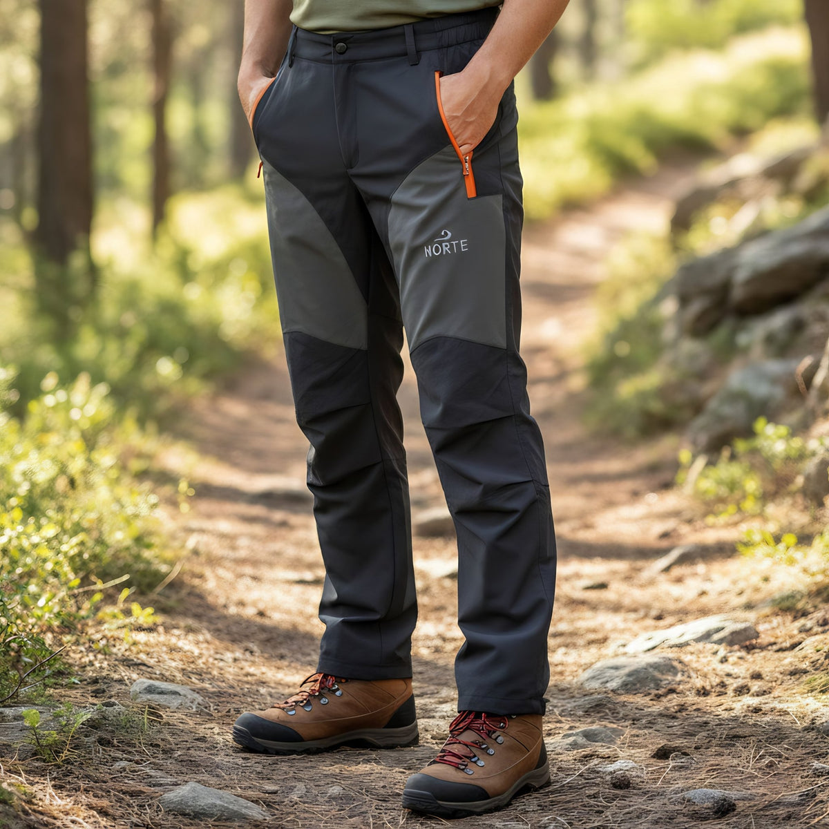 A person wearing the dark grey Norte Outdoors Ascent V4.0 men's hiking pants while standing on a dirt trail in a sunny forest setting.