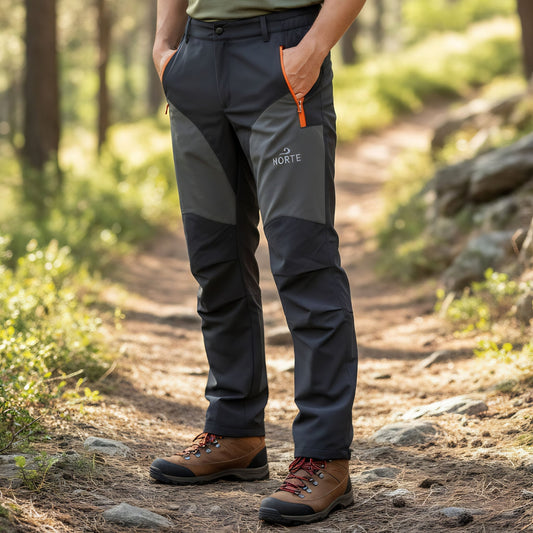 A person wearing the dark grey Norte Outdoors Ascent V4.0 men's hiking pants while standing on a dirt trail in a sunny forest setting.