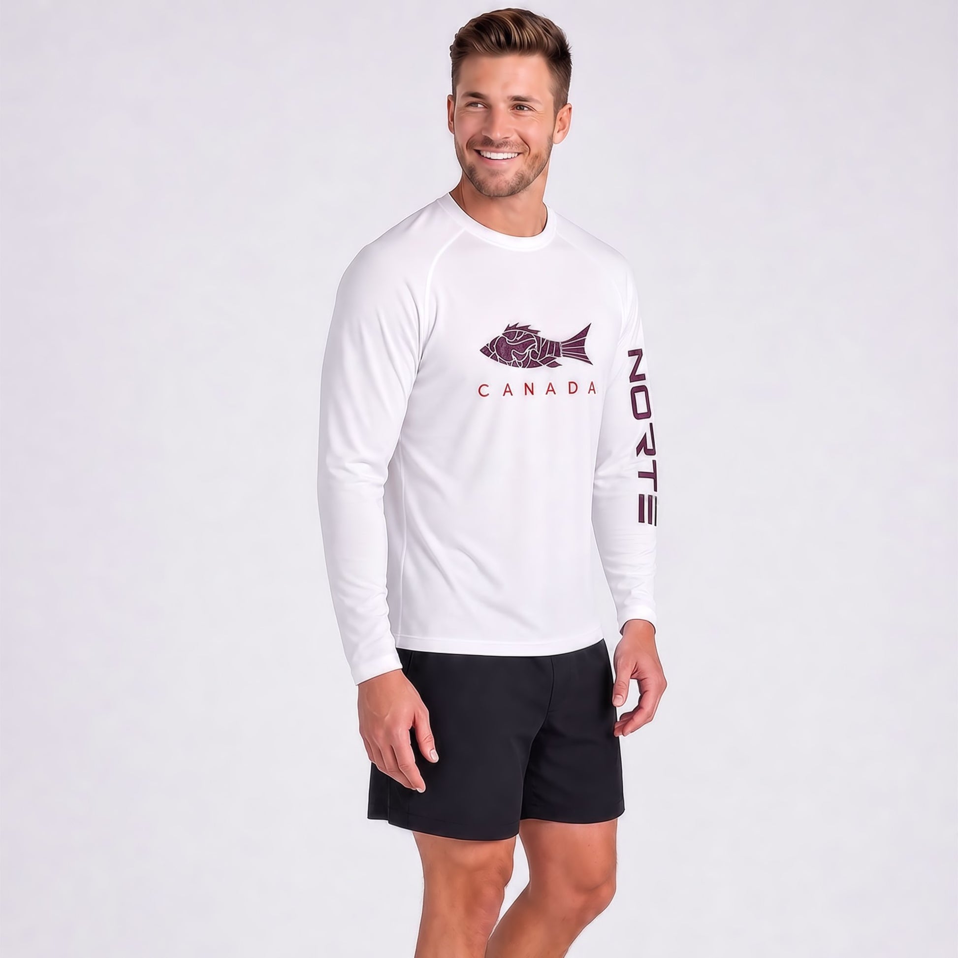 Smiling athletic man wearing Norte brand white long sleeve performance shirt with fish graphic and red CANADA text on the chest, paired with black shorts against a light gray background