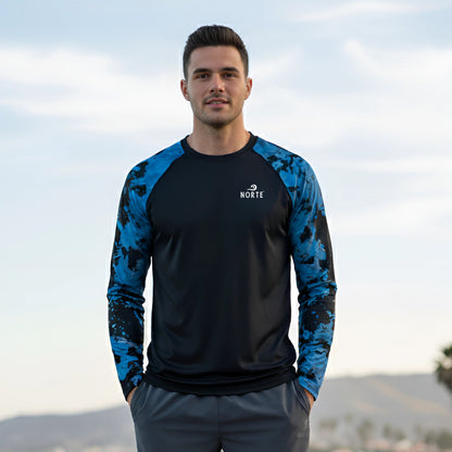 Model wearing the Norte® Coastal Drift adult performance rash guard in an outdoor coastal setting.