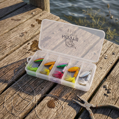 An open plastic tackle box containing five colorful inline spinner fishing lures resting on a weathered wooden dock next to fishing line and pliers.