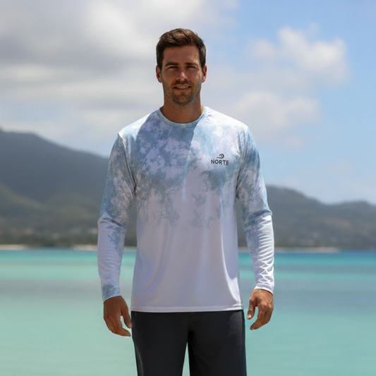 Model wearing the Norte Mist Flow Sun-Safe Fishing Shirt on a coastal beach, highlighting the relaxed performance fit and mist-blue tie-dye design.
