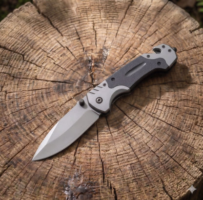 Norte Tactical Folding Knife with titanium-grey blade and textured G10 grip handle, resting on a wooden log to showcase its rugged outdoor survival design.