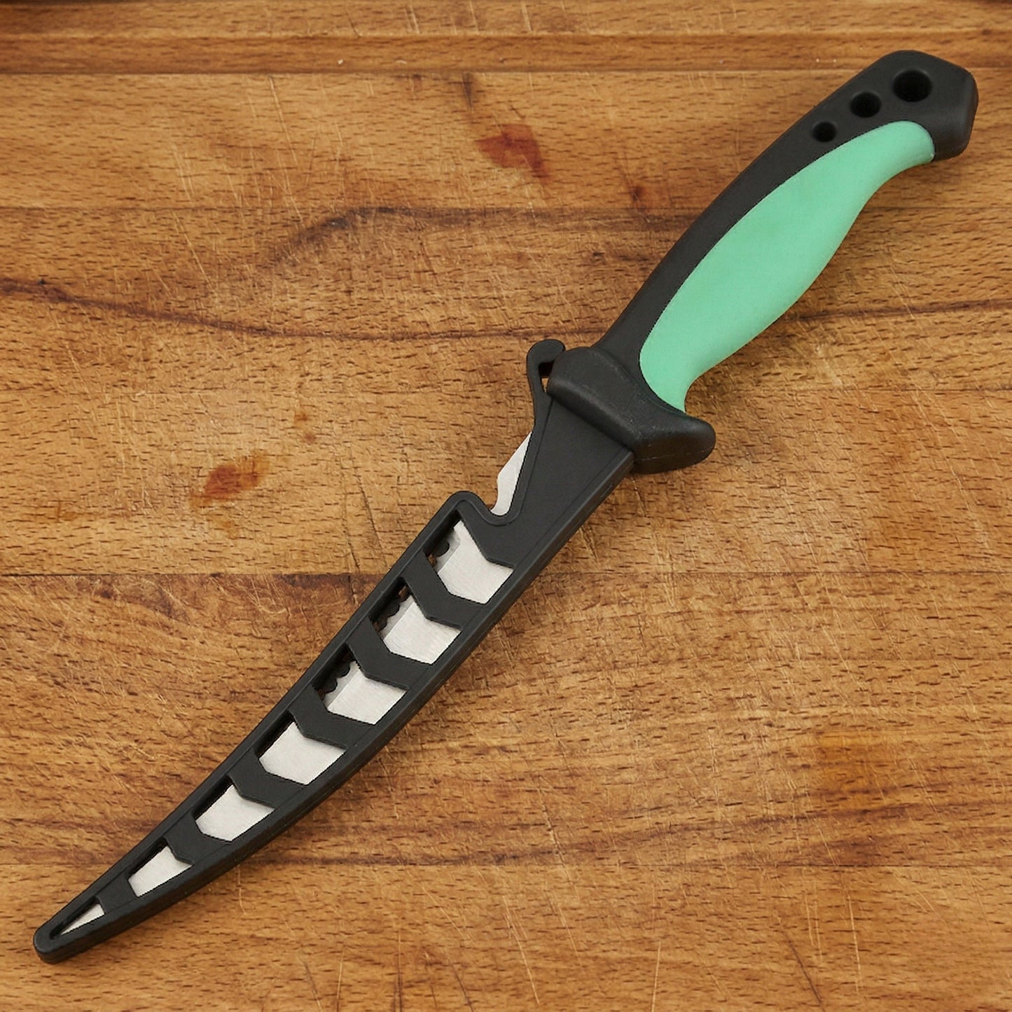 Norte Technical Fillet & Boning knife with a Forest Green handle shown inside its black ventilated protective sheath on a wooden surface.