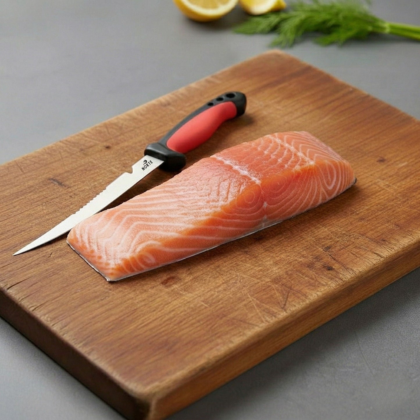 A fresh salmon fillet on a wooden cutting board next to the Norte Technical Fillet & Boning knife with a Crimson Red non-slip handle, illustrating precision kitchen and field food prep."