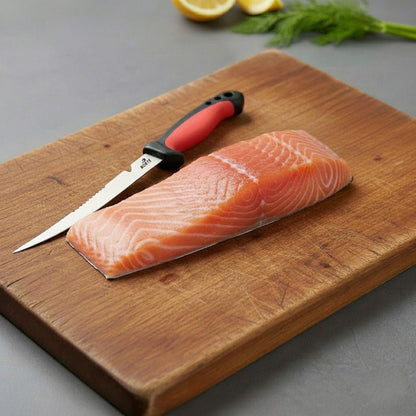 A fresh salmon fillet on a wooden cutting board next to the Norte Technical Fillet & Boning knife with a Crimson Red non-slip handle, illustrating precision kitchen and field food prep."