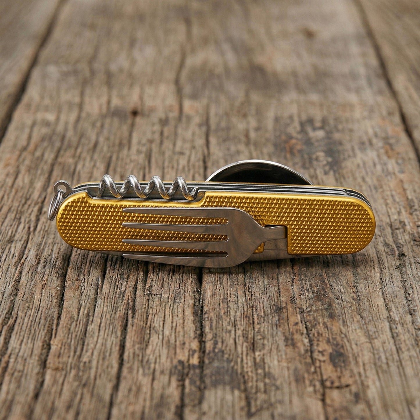 Close-up of a yellow 6-in-1 detachable camping multi-tool showing the integrated stainless steel fork and corkscrew on a rustic wooden table.