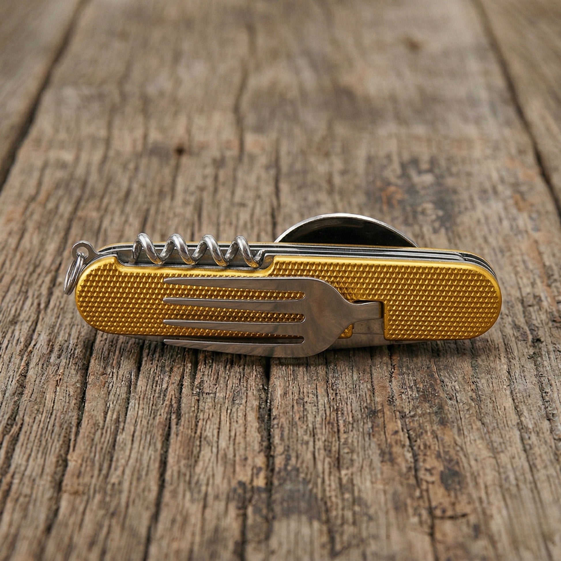 Close-up of a yellow 6-in-1 detachable camping multi-tool showing the integrated stainless steel fork and corkscrew on a rustic wooden table.